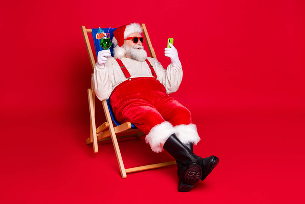 Portrait of his he nice handsome bearded fat Santa father hipster sitting in chair drinking mojito using device blog rest relax chill isolated bright vivid shine vibrant red color background - Фото, зображення