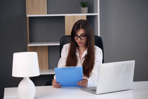 Young pretty brunette business woman with laptop in the office - 写真・画像
