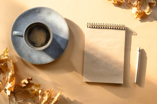 Autumn black coffee and empty sketchbook with copy space for design or sketch, writing plans and dreams on beige background with sunny shadow. Copy space. View from above. - Foto, Bild