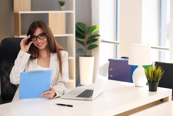 Mulher de negócios bonita usa um laptop e sorri enquanto trabalha no escritório - Foto, Imagem