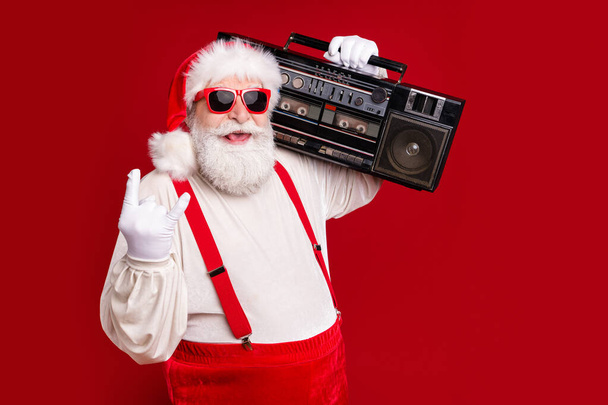 Portrait of his he handsome cool cheerful bearded Santa dj deejay hipster carrying boombox having fun showing horn sign swag leisure isolated bright vivid shine vibrant red color background - Foto, Imagen