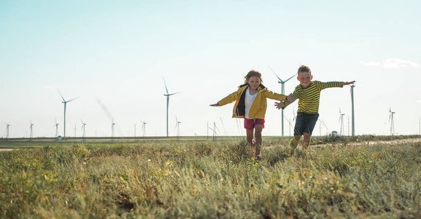Little girl and boy are running in front of windmills. Renewable energies and sustainable resources - wind mills. children playing with the wind near a wind turbine. - Photo, Image