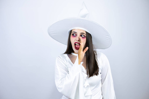 Woman wearing witch costume over isolated white background hand on mouth telling secret rumor, whispering malicious talk conversation - Photo, Image