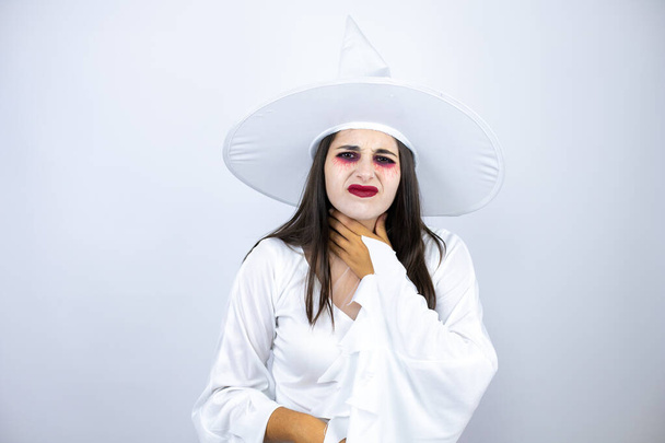 vrouw dragen heks kostuum over geïsoleerde witte achtergrond aanraken pijnlijke nek, zere keel voor griep, clod en infectie - Foto, afbeelding