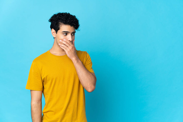 Young Venezuelan man isolated on blue background doing surprise gesture while looking to the side - Foto, Bild