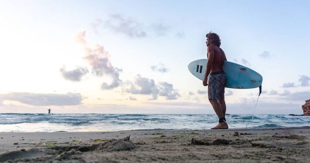 Joven caucásico hombre levantarse temprano a hacer surf al amanecer - Foto, imagen