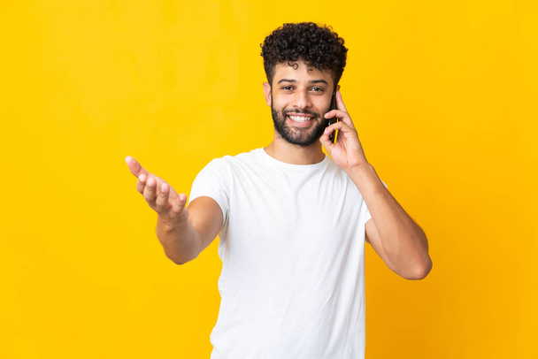 Young Moroccan man isolated on yellow background keeping a conversation with the mobile phone with someone - Foto, Bild