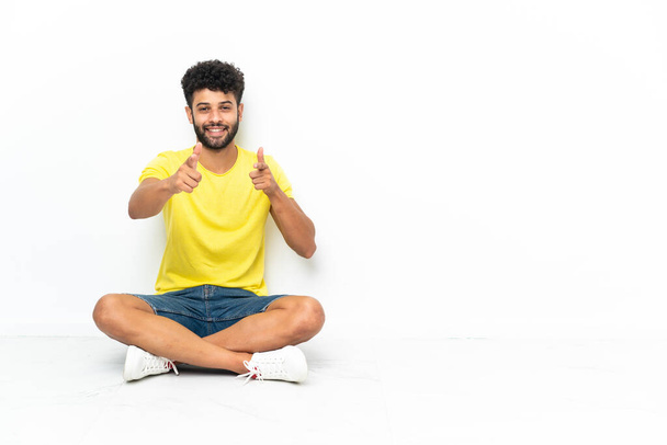 Young Moroccan handsome man sitting on the floor over isolated background pointing to the front and smiling - Photo, Image