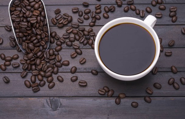 Dunkler Kaffee in einer weißen Kaffeetasse und geröstete Kaffeebohnen auf einem schwarzen Holztisch und Platz für Textgestaltung. - Foto, Bild