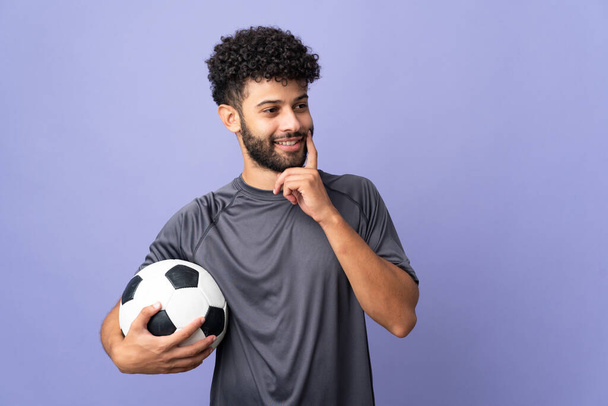Guapo marroquí joven futbolista hombre sobre aislado en púrpura fondo pensando una idea mientras mira hacia arriba - Foto, imagen