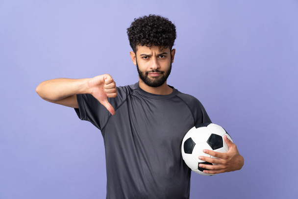 Guapo marroquí joven futbolista hombre sobre aislado en púrpura fondo mostrando pulgar hacia abajo con expresión negativa - Foto, imagen
