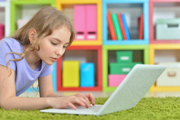 Симпатична дівчина використовує ноутбук, лежачи на зеленій підлозі вдома
 - Фото, зображення