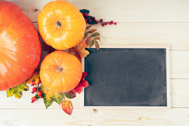 カボチャ、果実、落ち葉はチョークで木製の背景に黒板のフレームをモックします。テキストのスペースをコピーします。ハロウィーン、感謝祭の日または季節の秋。フラットレイアウト、トップビューデザイン - 写真・画像
