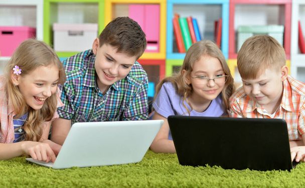 Group of children lying on floor with green carpet and looking at modern laptops - Foto, Bild