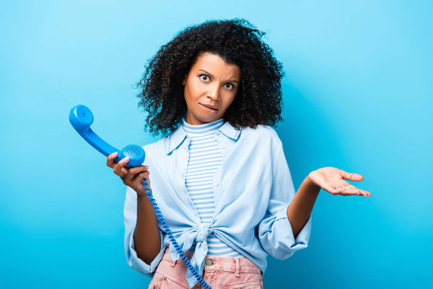confused african american woman holding retro phone on blue - Photo, Image