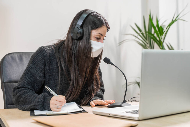 Telemarketer woman working on laptop and talking on a headset with face mask at office. Self employed and working from home because of coronavirus. Business worker answer customer calls.  - Foto, Bild
