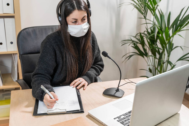 Telemarketer woman working on laptop and talking on a headset with face mask at office. Self employed and working from home because of coronavirus. Business worker answer customer calls.  - Photo, image