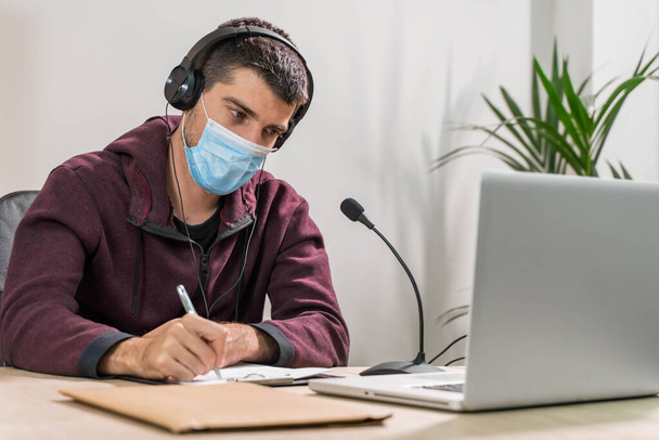 Telemarketer man working on laptop and talking on a headset with face mask at office. Self-isolated and working from home because of coronavirus. Business worker answer customer calls.  - Φωτογραφία, εικόνα
