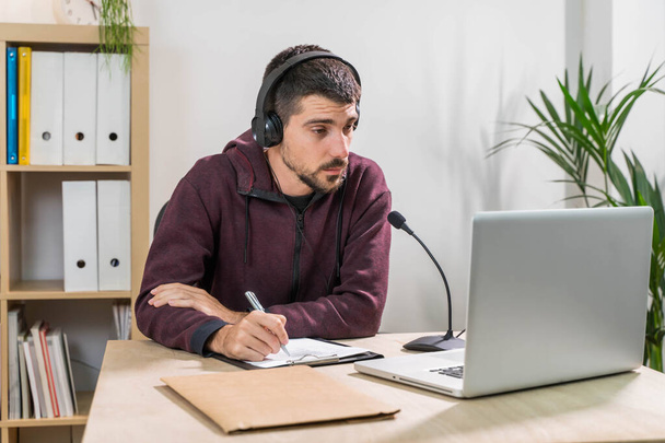 Telemarketer man working on laptop and talking on a headset with face mask at office. Self-isolated and working from home because of coronavirus. Business worker answer customer calls.  - Foto, Imagem