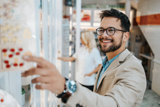 Young business man buying some drugs in a drugstore or pharmacy while attractive female pharmacist working something in background.  - Photo, image