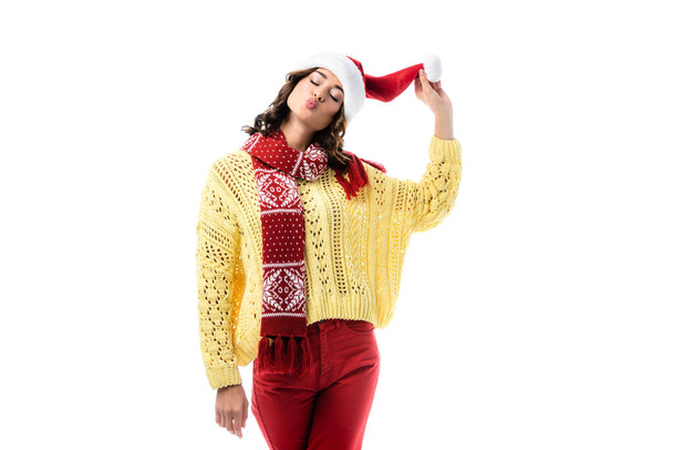 young woman with duck face and closed eyes touching santa hat isolated on white - Fotó, kép