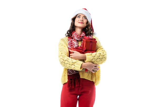 dreamy young woman in santa hat and scarf holding gifts isolated on white - Photo, Image