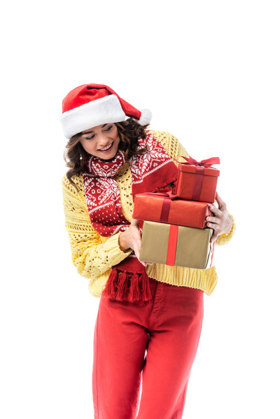 zufriedene junge Frau mit Weihnachtsmütze und Schal beim Betrachten von Geschenken auf weißem Grund - Foto, Bild