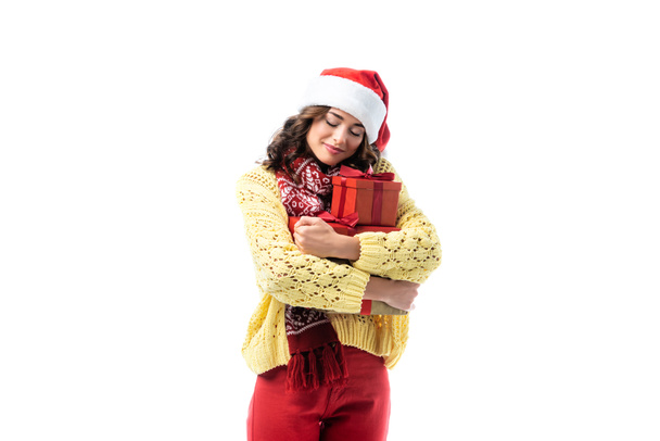 joyful young woman in santa hat and scarf embracing gifts isolated on white - Foto, immagini