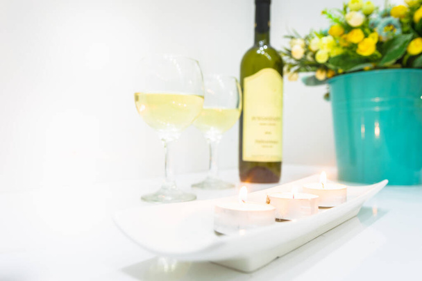 Setup on table of white wine bottle with two glasses and bucket of flowers on on corner. Romantic bright blank space background. - Photo, Image