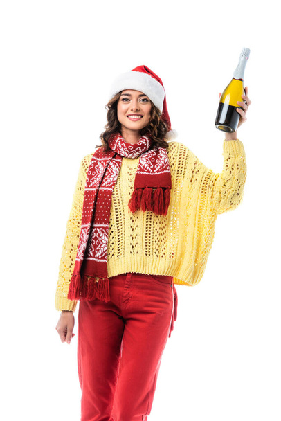 joyful young woman in santa hat and scarf with ornament holding bottle of champagne isolated on white  - Фото, изображение