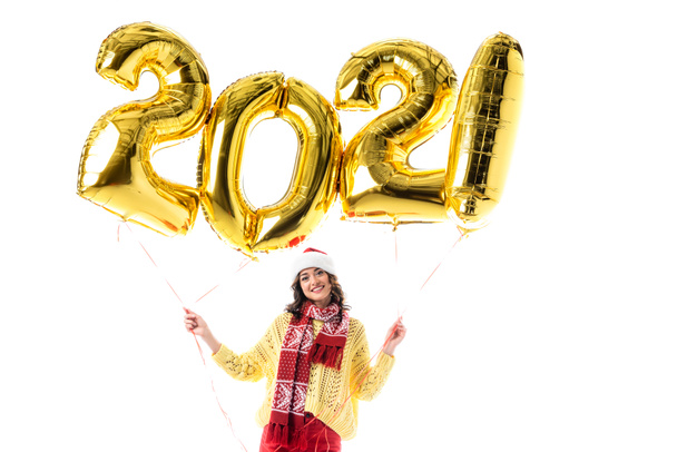 joyful young woman in santa hat and scarf holding balloons with 2021 numbers isolated on white - Foto, Imagen