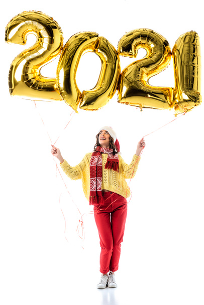 joyful young woman in santa hat and scarf holding balloons with numbers isolated on white - Fotó, kép