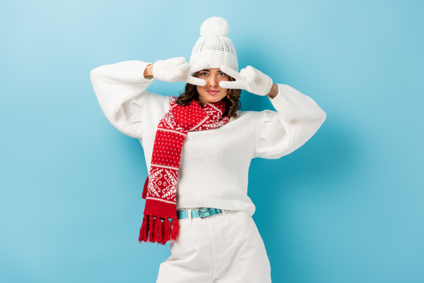 young woman in white winter outfit showing peace sign on blue  - Foto, Bild