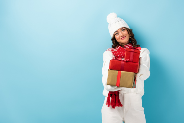 young joyful woman in winter outfit holding presents on blue - Photo, image