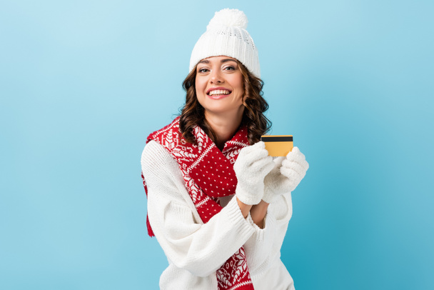 happy woman in winter outfit holding credit card on blue - Photo, Image