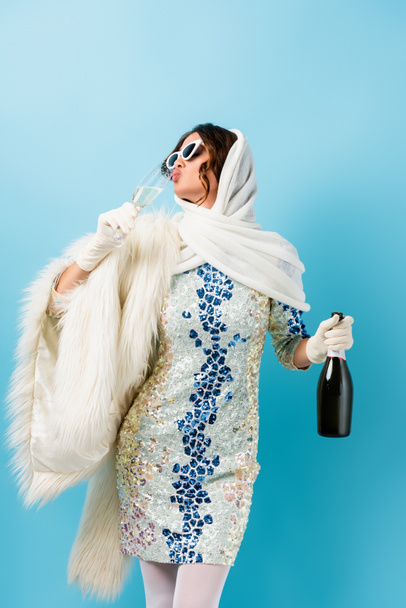 stylish woman in sunglasses holding bottle and drinking champagne on blue - Valokuva, kuva