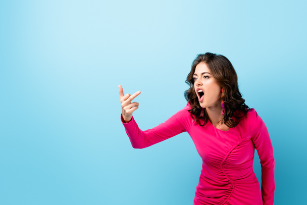 displeased young woman showing middle finger and screaming on blue  - Photo, Image