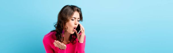 recorte horizontal de mujer morena gritando mientras habla en el teléfono inteligente y el gesto en azul - Foto, Imagen