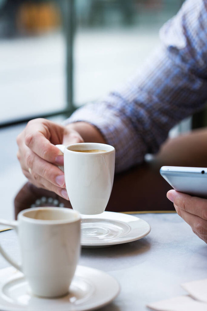 Jonge succesvolle zakenman zit in een café, het drinken van koffie in de ochtend en het gebruik van de smartphone. Lifestyle compositie met natuurlijk licht  - Foto, afbeelding