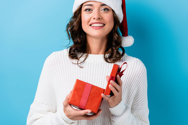 young cheerful woman holding gift box on blue - Foto, imagen