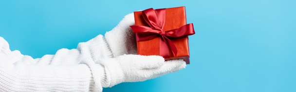 panoramic crop of woman in gloves holding gift box on blue - Photo, Image