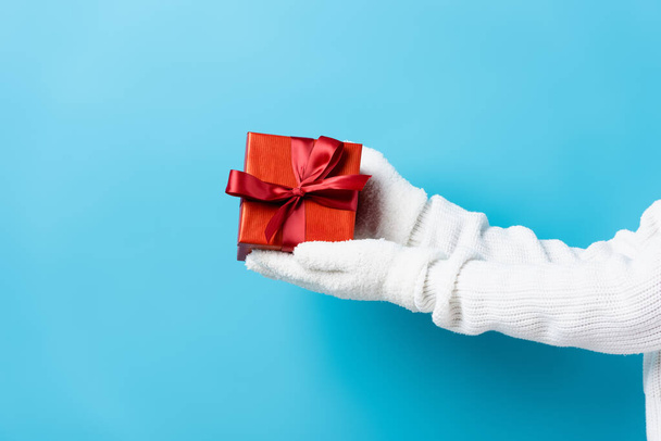 cropped view of young woman in gloves holding gift box on blue - Fotografie, Obrázek