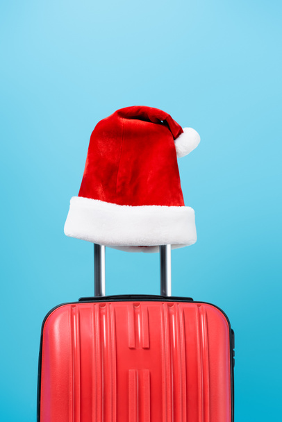 red santa hat on modern travel bag isolated on blue  - Zdjęcie, obraz