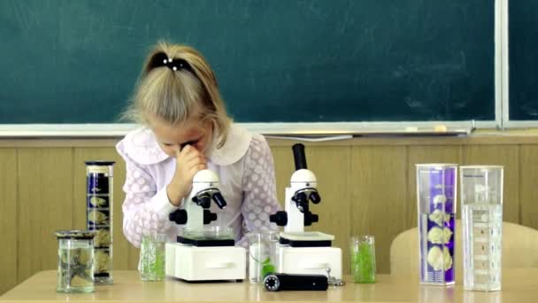 Menina perto do microscópio na sala de aula, quadro-negro no fundo. Primeiro ex-interessado em estudar, aprender, educação. Conceito de aluno entusiasmado. Criança, pupila no rosto calmo perto do microscópio. - Filmagem, Vídeo