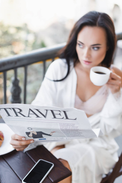 brunette woman in white robe sitting on balcony and reading newspaper - Photo, Image