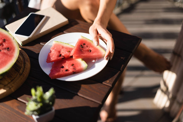 abgeschnittene Ansicht einer Frau, die Wassermelonenscheibe vom Teller nimmt - Foto, Bild