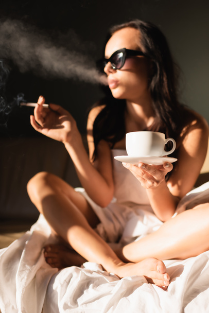 sexy brunette vrouw bedekt met wit laken roken sigaret en het drinken van koffie - Foto, afbeelding