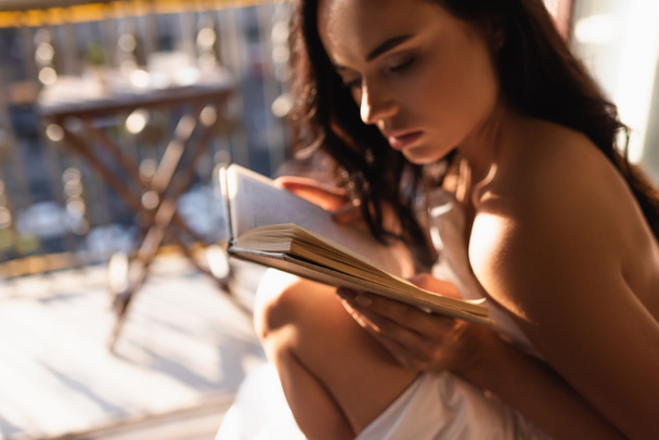 attractive woman covered in white sheet reading book and sitting on balcony - Photo, Image