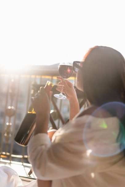 ブルネットの女性でサングラスと白いシャツはバルコニーでワインを飲む - 写真・画像