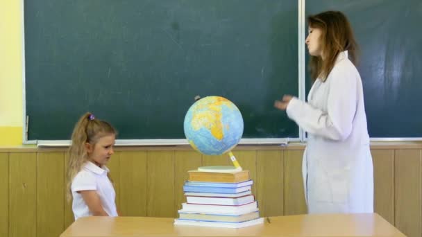 Ein junger Lehrer schimpft den Schüler in der Schule auf dem Hintergrund der Tafel. auf dem Tisch Bücher und Globus. - Filmmaterial, Video
